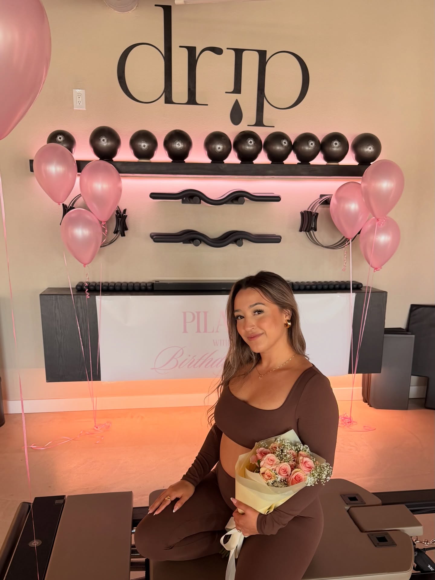 Founder Sarah Franco at the Drip Pilates studio, in front of the brand wordmark on the studio wall.